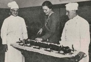 Het aansnijden van een groot Driekoningenbrood dat omringd is door 12 kaarsjes,1932